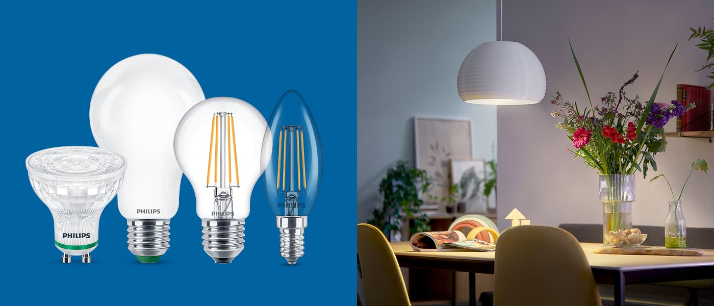 Fire Philips LED-lyspærer mot blå bakgrunn og koselig belysning over et spisebord med blomster og bøker.