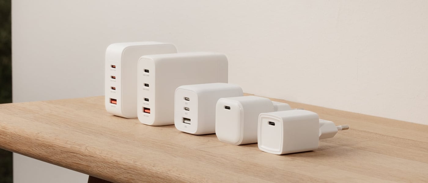 Fem vita USB-väggladdare i olika storlek och kapacitet uppradade på ett träbord mot ljus bakgrund.