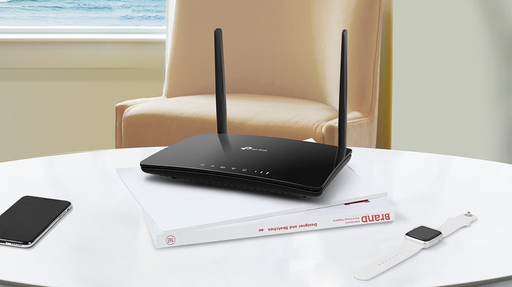 Svart ruter med to antenner plassert på en bok, ved siden av en smartklokke og en smarttelefon på et hvitt bord.