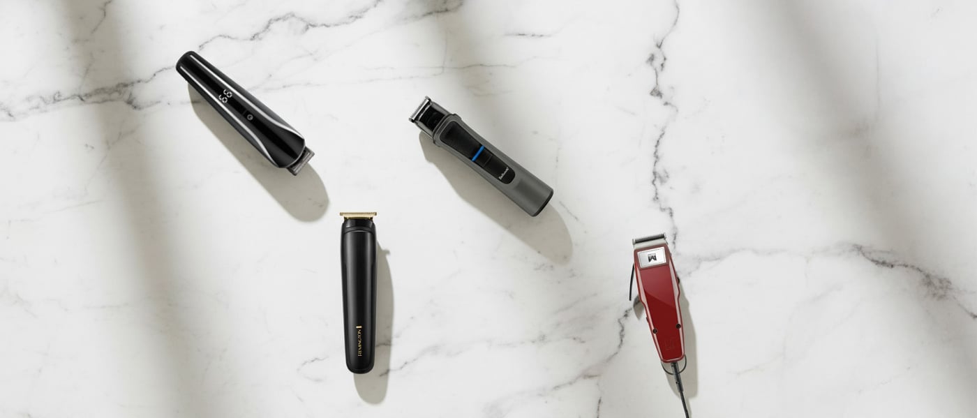 Svart och guldfärgad Remington-trimmer med tillbehör och kam, placerade mot ett mönstrat svartvitt underlag.