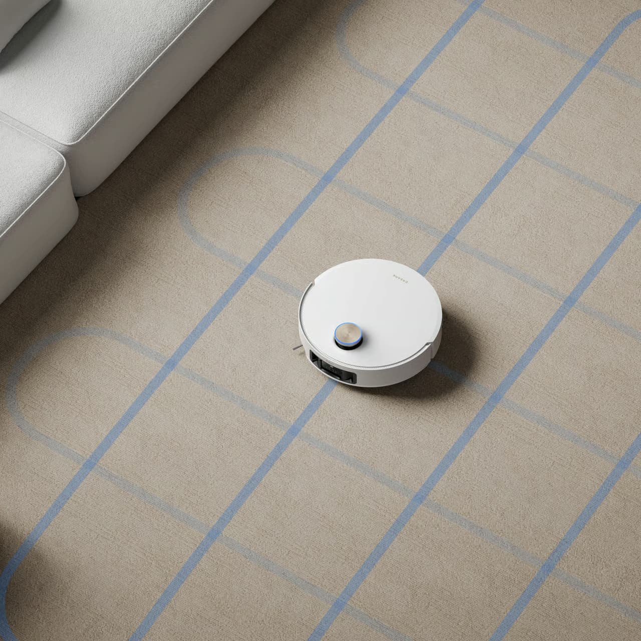 Robotdammsugare navigerar systematiskt på matta med blå rutnät, intill ljusgrå soffa.