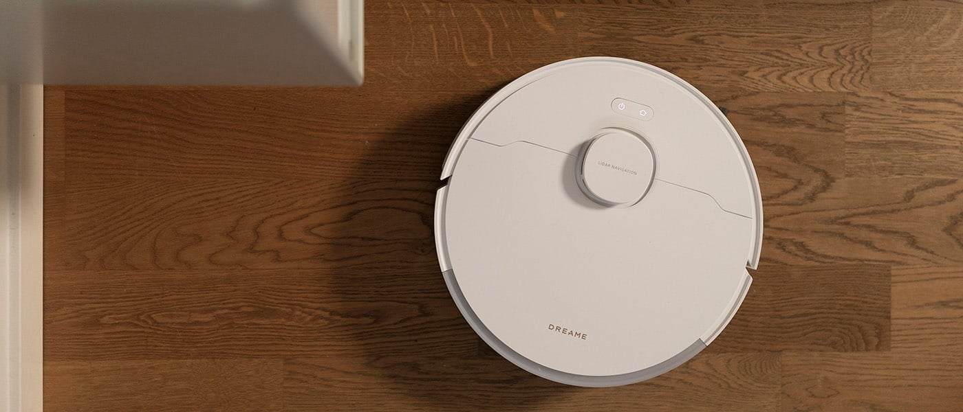 Vit robotdammsugare från Dreame rengör ett golv i trä med tydlig ådring.