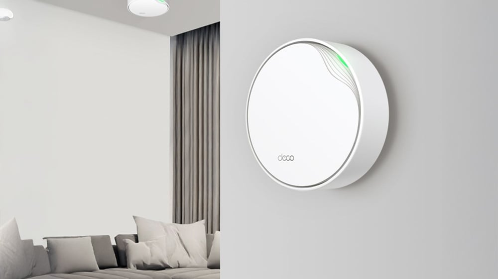 Hvit, rund WiFi-enhet med grønt indikatorlys montert på vegg i en moderne stue.