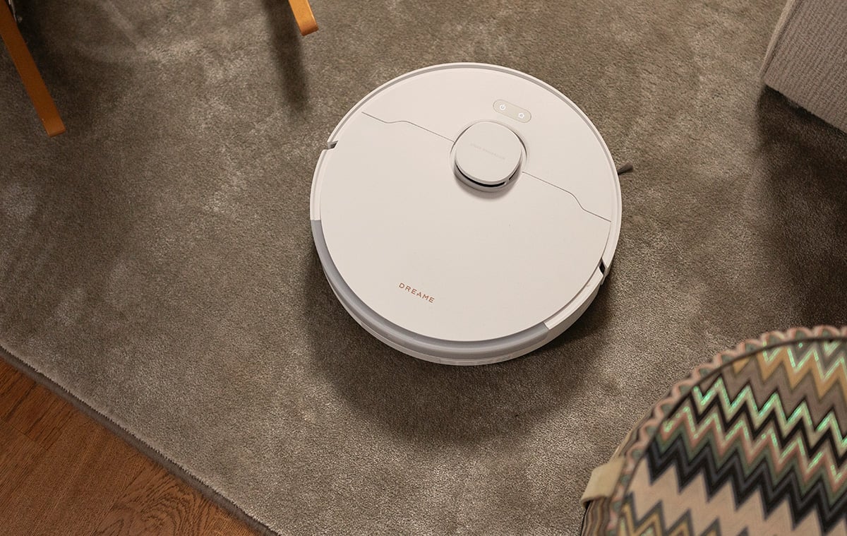 Vit robotdammsugare som kör på en grå matta.