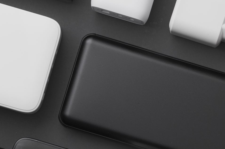 Nærbilde av flere svarte og hvite powerbanks med avrundede kanter, arrangert på mørk bakgrunn.