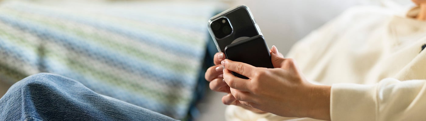 Person håller en smartphone med ett svart magnetiskt powerbank-fodral medan hen sitter avslappnat i soffa.