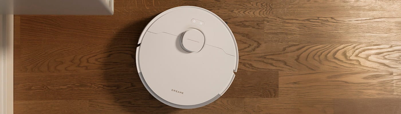 Vit robotdammsugare från Dreame rengör ett golv i trä med tydlig ådring.