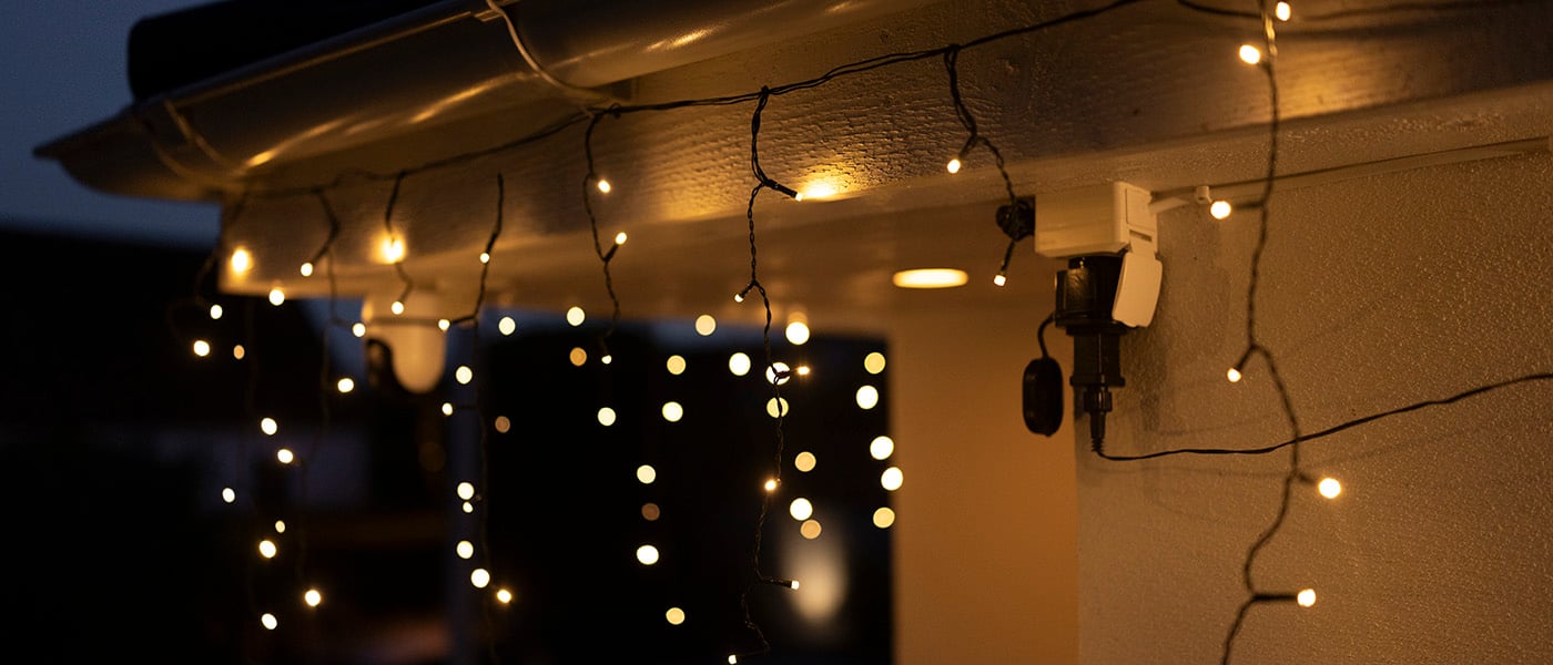 Varmhvit lyslenke med istappeffekt hengende fra takrenne, tent i mørket i utendørsmiljø.