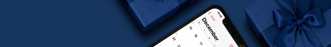 Smartphone med kalender inställd på december 2025, omgiven av mörkblå presentaskar med rosetter.