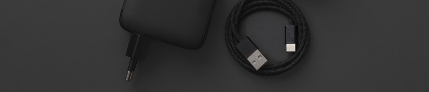 Svart USB-laddare och flätad USB-C-kabel mot mörkgrå bakgrund