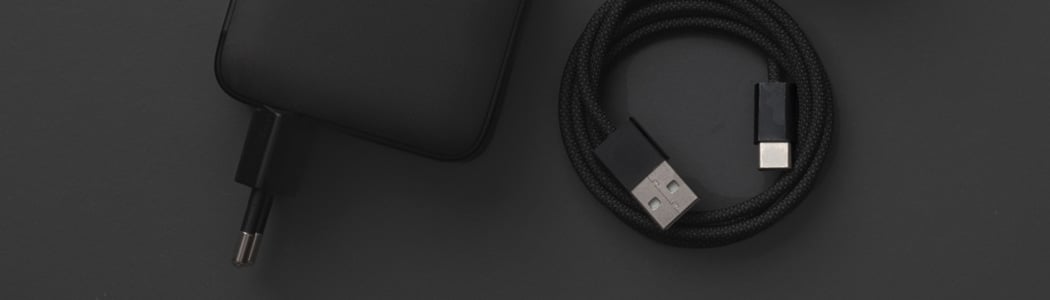 Svart USB-lader og flettet USB-C-kabel mot mørkegrå bakgrunn