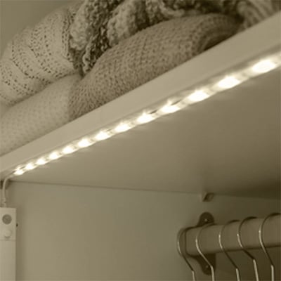 LED-ljusslinga monterad under en hylla i garderob, med vikta filtar ovanpå och klädhängare under.