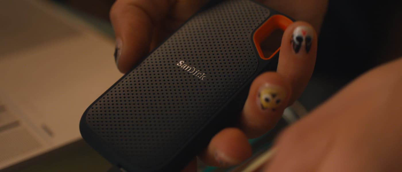 Person håller en kompakt, svart SanDisk extern SSD med orange kant och perforerat mönster.