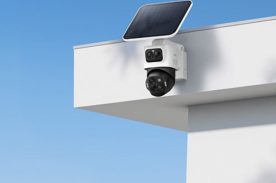 Eufy dubbellins övervakningskamera med solpanel monterad på hustak mot blå himmel.
