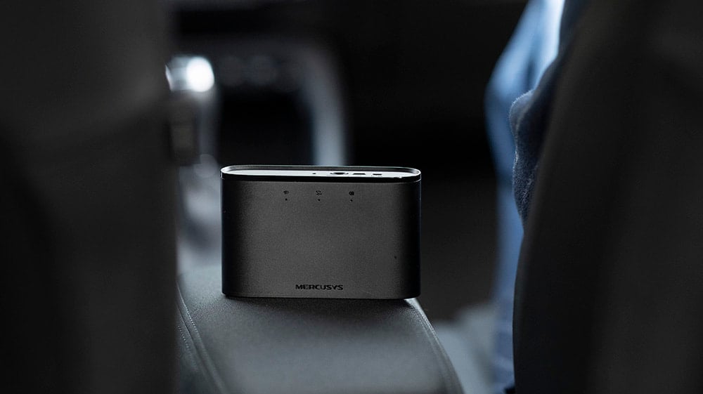 Svart trådløs ruter fra Mercusys plassert på et bilsete, med LED-lamper på forsiden.