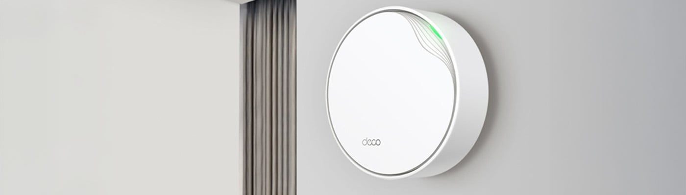 Vit rund WiFi-router från Deco monterad på grå vägg, med grönt ljus, i modern vardagsrumsmiljö.