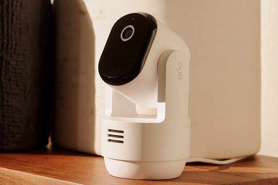 Arlo innendørskamera med bevegelig linse plassert på en trehylle.
