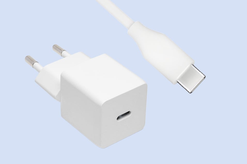 Hvit vegglader med USB-C-port og tilhørende hvit USB-C-kabel mot blå bakgrunn.