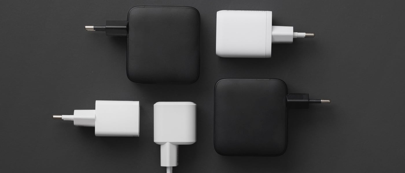 Svarta och vita USB-laddare med väggkontakt, liggande i rutmönster på mörk bakgrund.