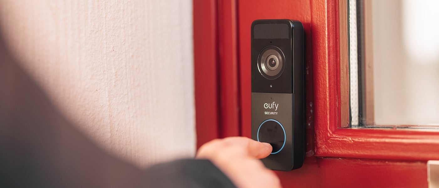 Eufy Security videodörrklocka monterad på röd dörrkarm, person trycker på knapp med blå LED-ring