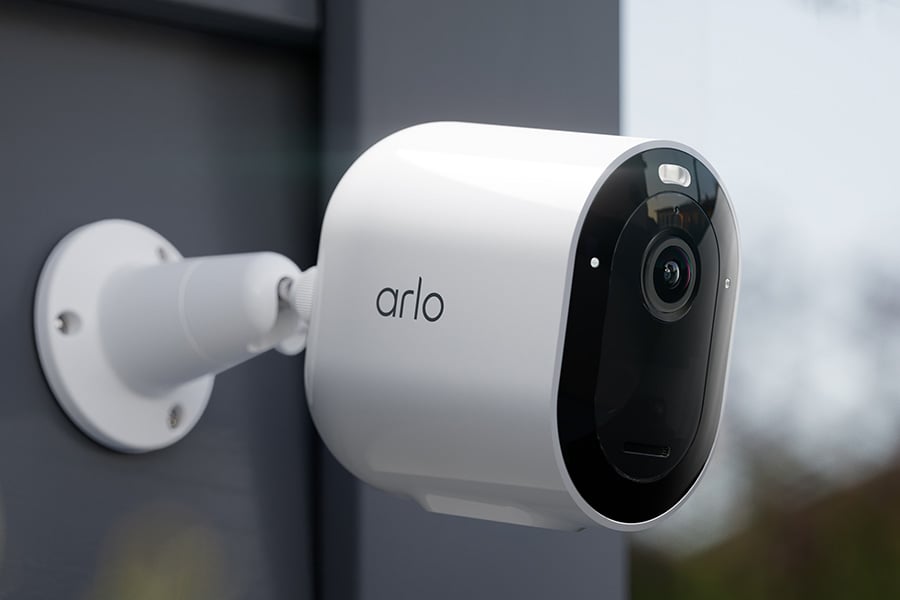 Vit Arlo-övervakningskamera monterad på yttervägg, med svart front och lins riktad framåt.