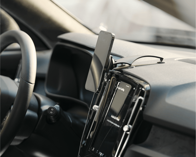 Smartphone monterad i magnetiskt bilfäste på bilens instrumentpanel, ansluten med laddkabel.