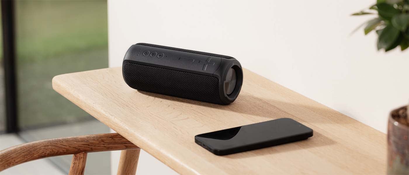 Svart portabel Bluetooth-högtalare och smartphone på ett träbord i hemmiljö.