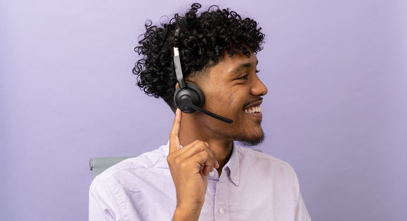 Svart powerbank med två USB-portar laddar en smartphone via kabel på ett ljust bord, suddig person i bakgrunden.