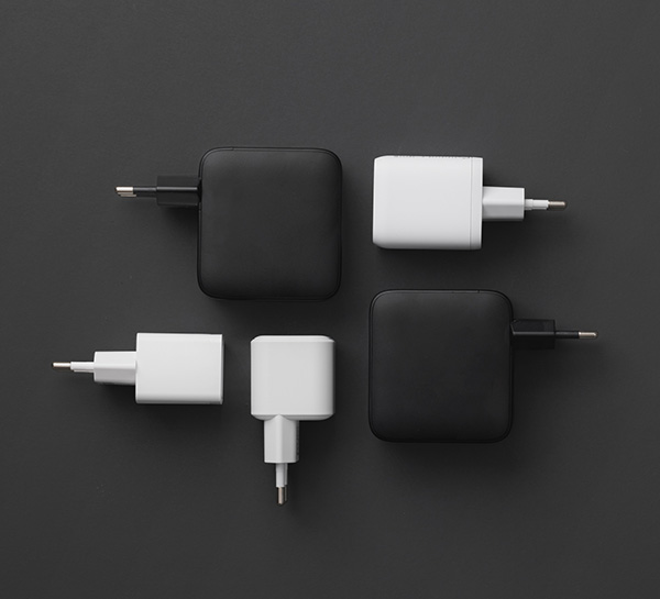 Fyra nätadaptrar i svart och vitt, fyrkantiga och rektangulära, placerade symmetriskt mot mörk bakgrund.