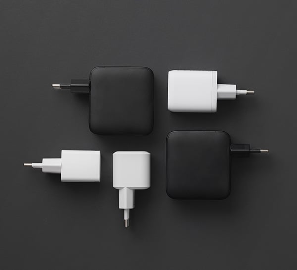 Fyra nätadaptrar i svart och vitt, fyrkantiga och rektangulära, placerade symmetriskt mot mörk bakgrund.