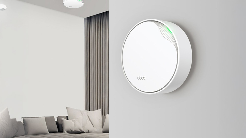 Vit, rund WiFi-enhet med grön indikatorlampa monterad på vägg i ett modernt vardagsrum.